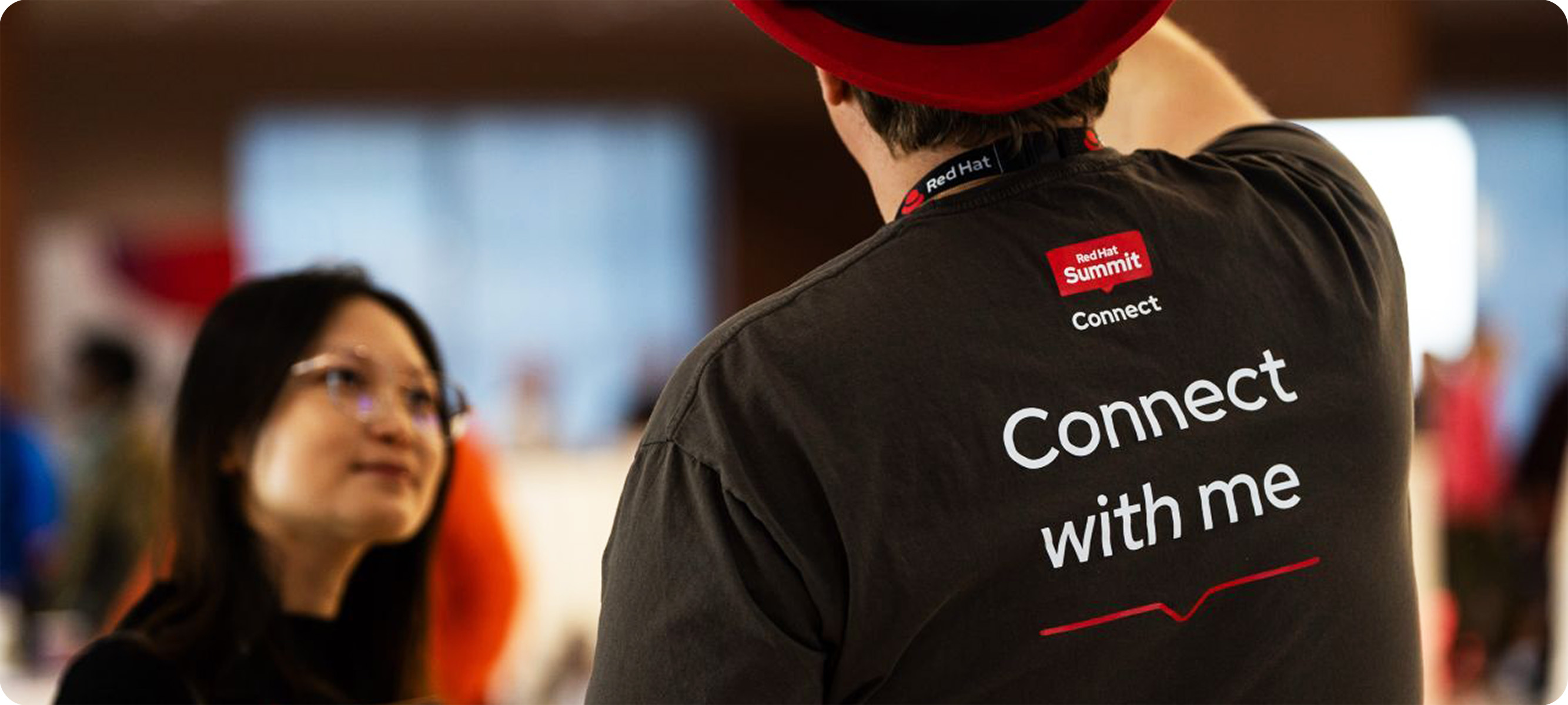 A man wears a lanyard with the Red Hat logo and a t-shirt with the Red Hat Summit: Connect logo on the nape.