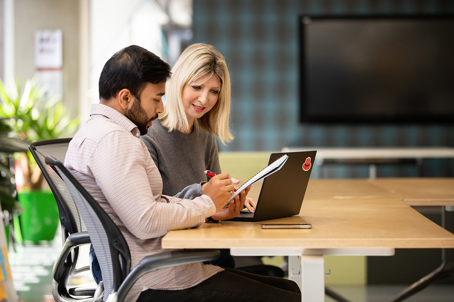 A photo of two Red Hatters talking at a computer.