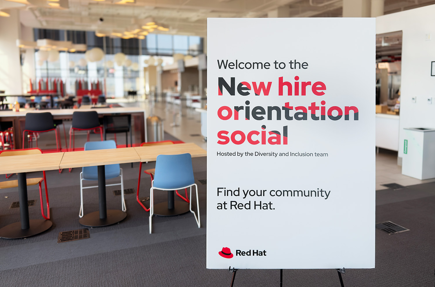 A photo shows a poster advertising a New Hire Orientation social. The text on the poster has been used as a mask with the hat placed inside of the mask, as though the viewer is looking through the letters at the hat behind them.
