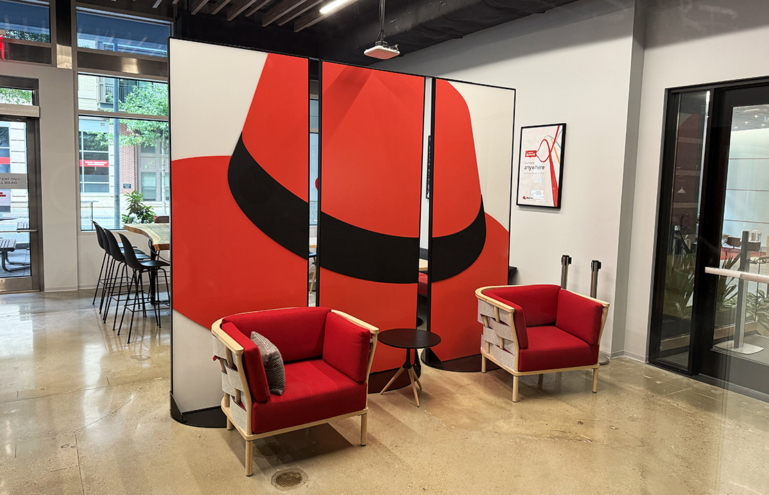A photo of a divider wall at Red Hat tower with the hat printed across 3 panels.