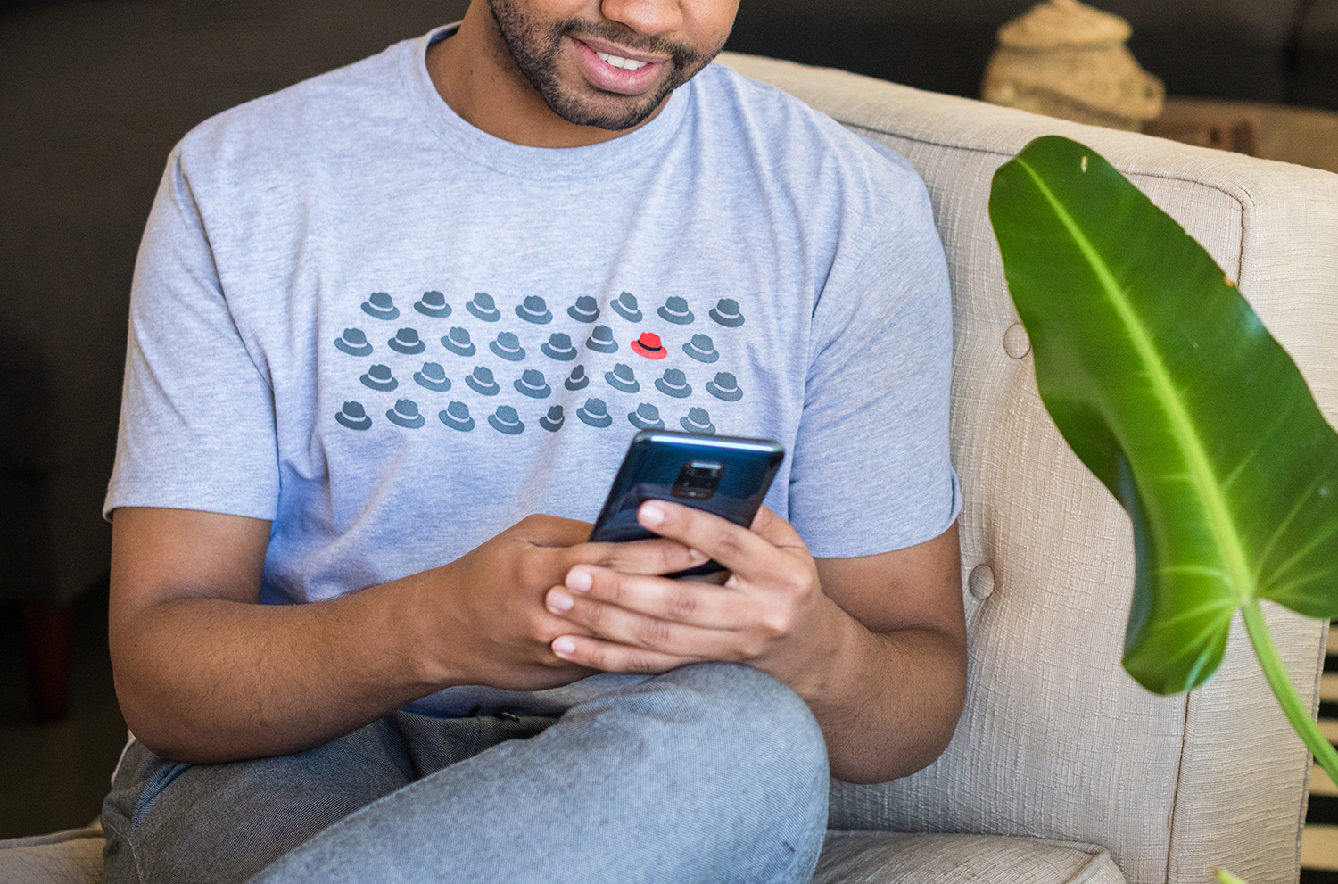 A photo shows a man wearing a t-shirt from the Red Hat Cool Stuff Store featuring a pattern of hats. All of the hats are one-color gray except for one, which is in full color. The full Red Hat logo is printed on the back of the shirt.