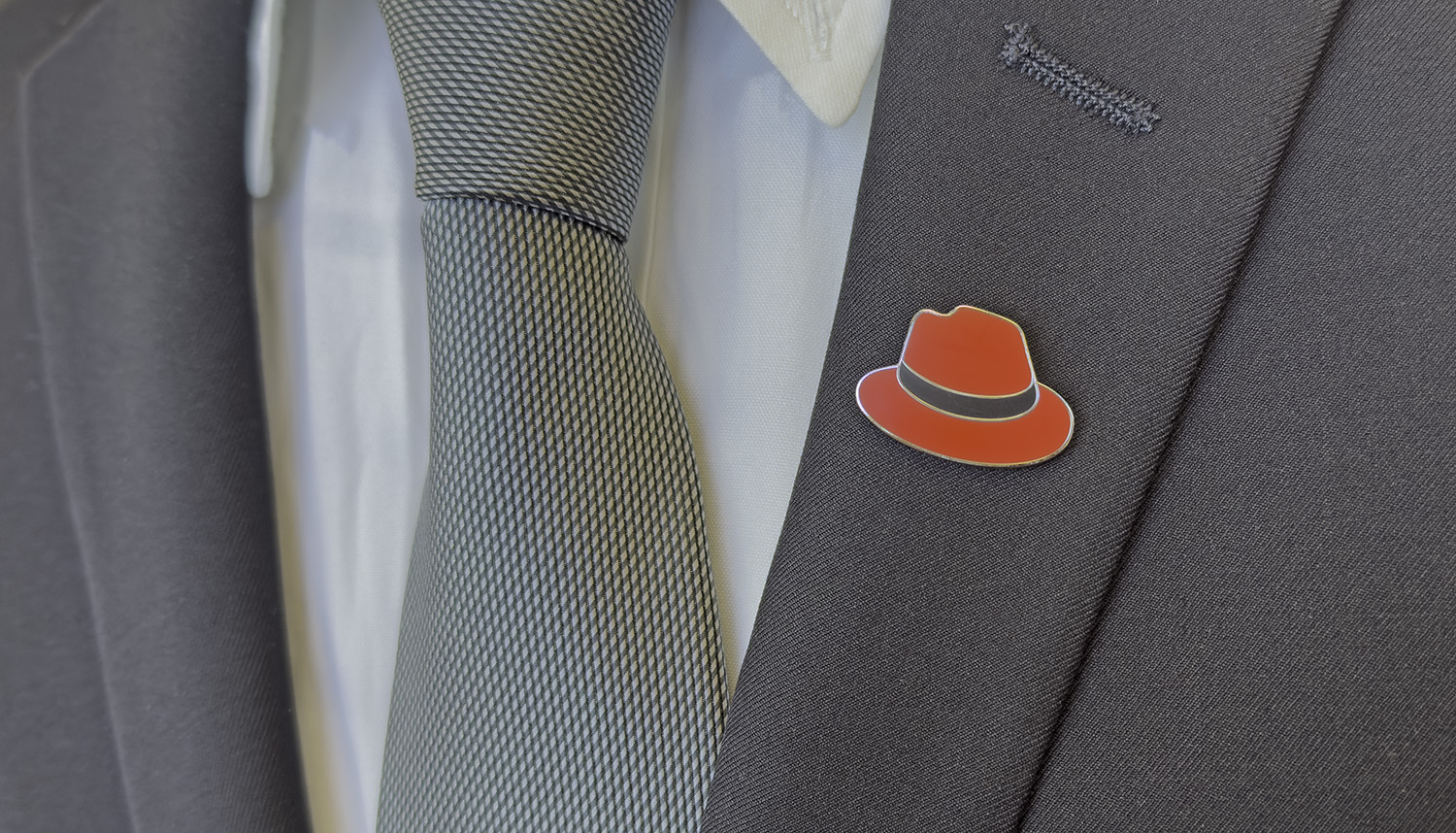 A photo shows a lapel pin of the hat on a suit jacket.