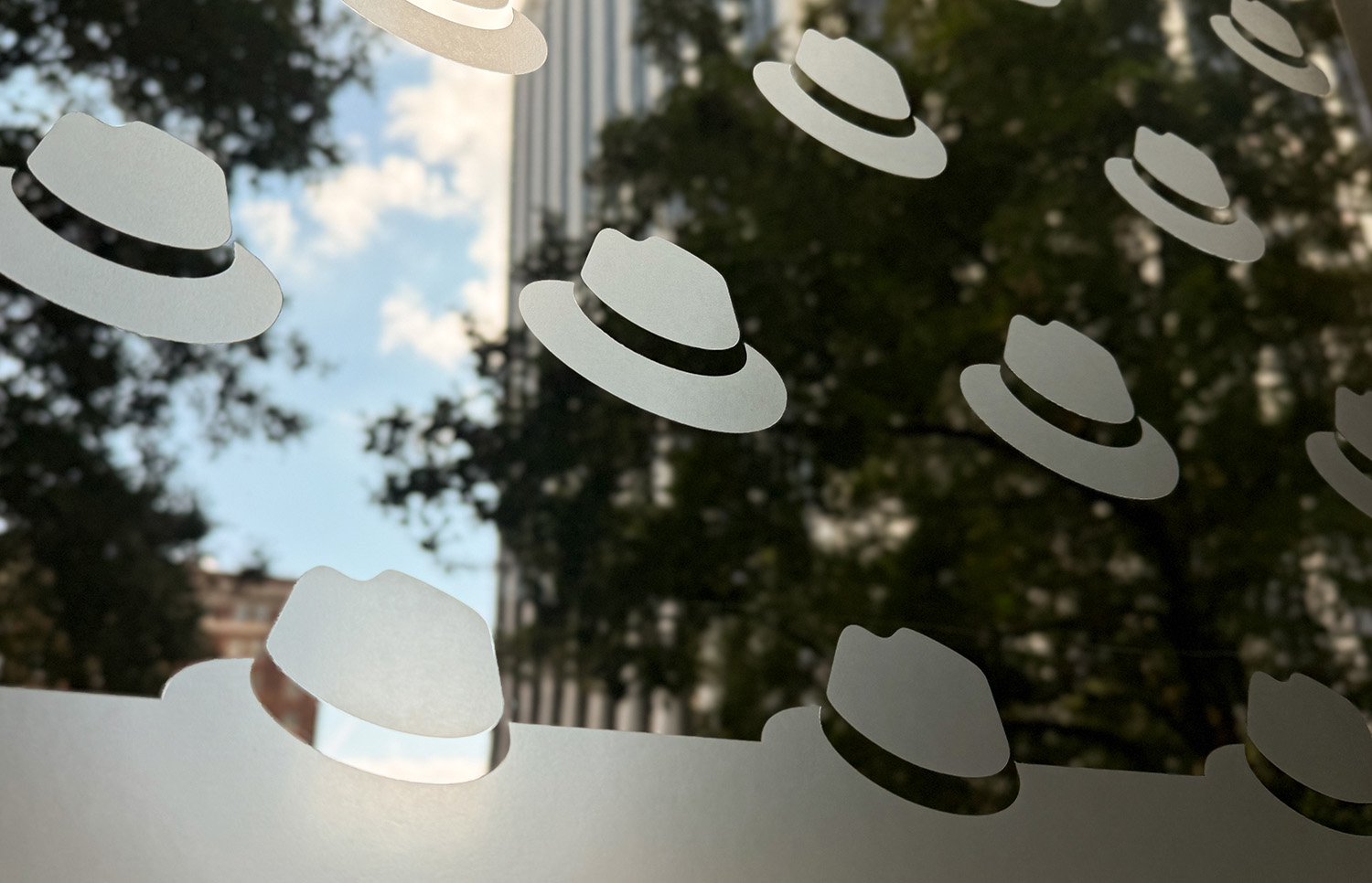 A photo shows a privacy cling on a window at a Red Hat office. The cling features a pattern of hats in one-color gray.
