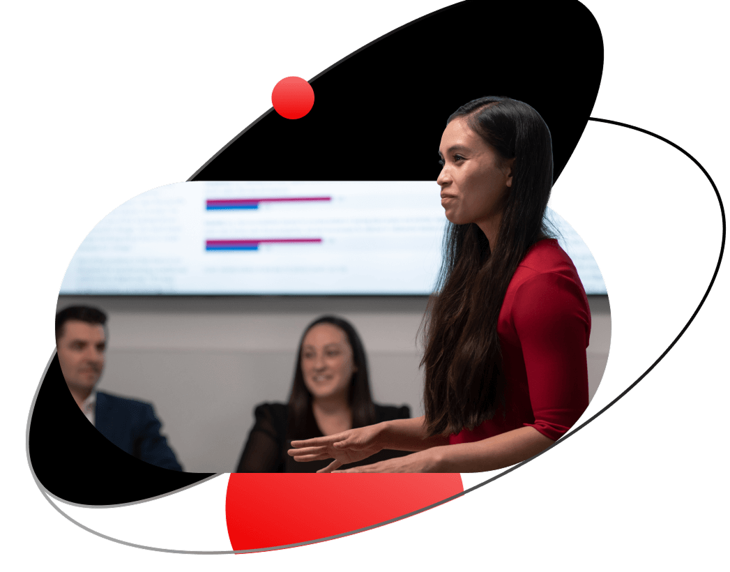 A woman in a red shirt presents to colleagues, framed by a stylized black orbit