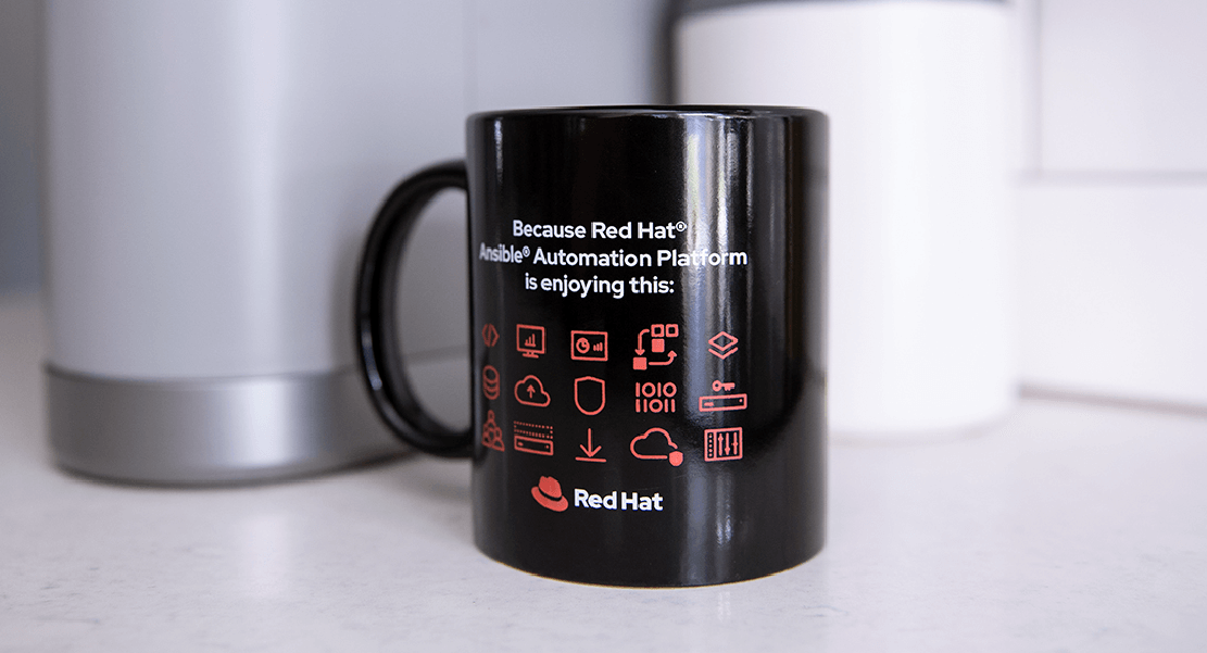 A black mug sitting on a kitchen counter. The mug features the Red Hat Ansible Automation Platform product logo and a grid of automation-related icons.
