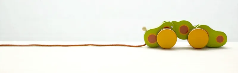 A photograph of a green and yellow wooden toy caterpillar with a red string attached for pulling it along.